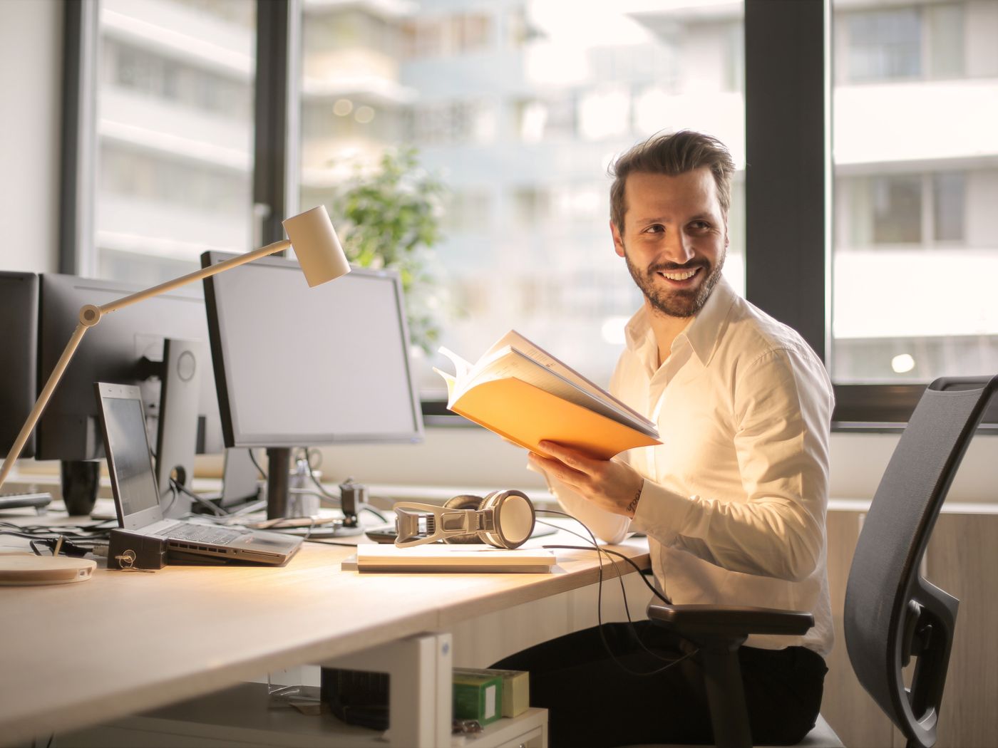 Freelancer sonriendo en su escritorio con laptop y monitores